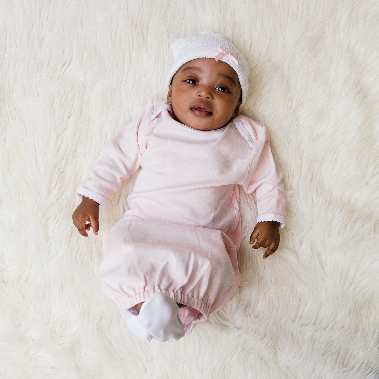 a baby in a pink Paty Knit Cap outfit laying on a white blanket from Paty.