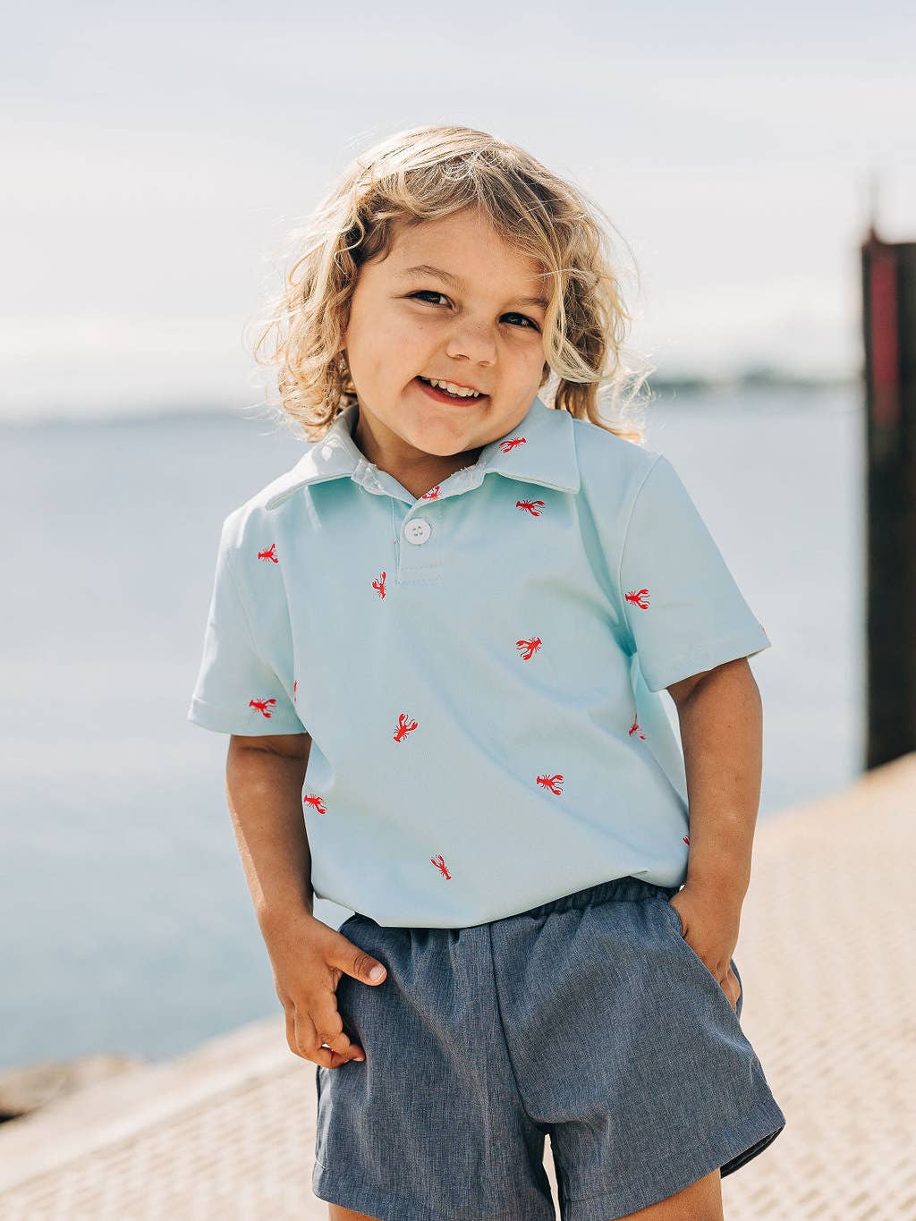 a little girl that is standing up by the water wearing a Sugar Bee Clothing Crawfish Polo Shirt.