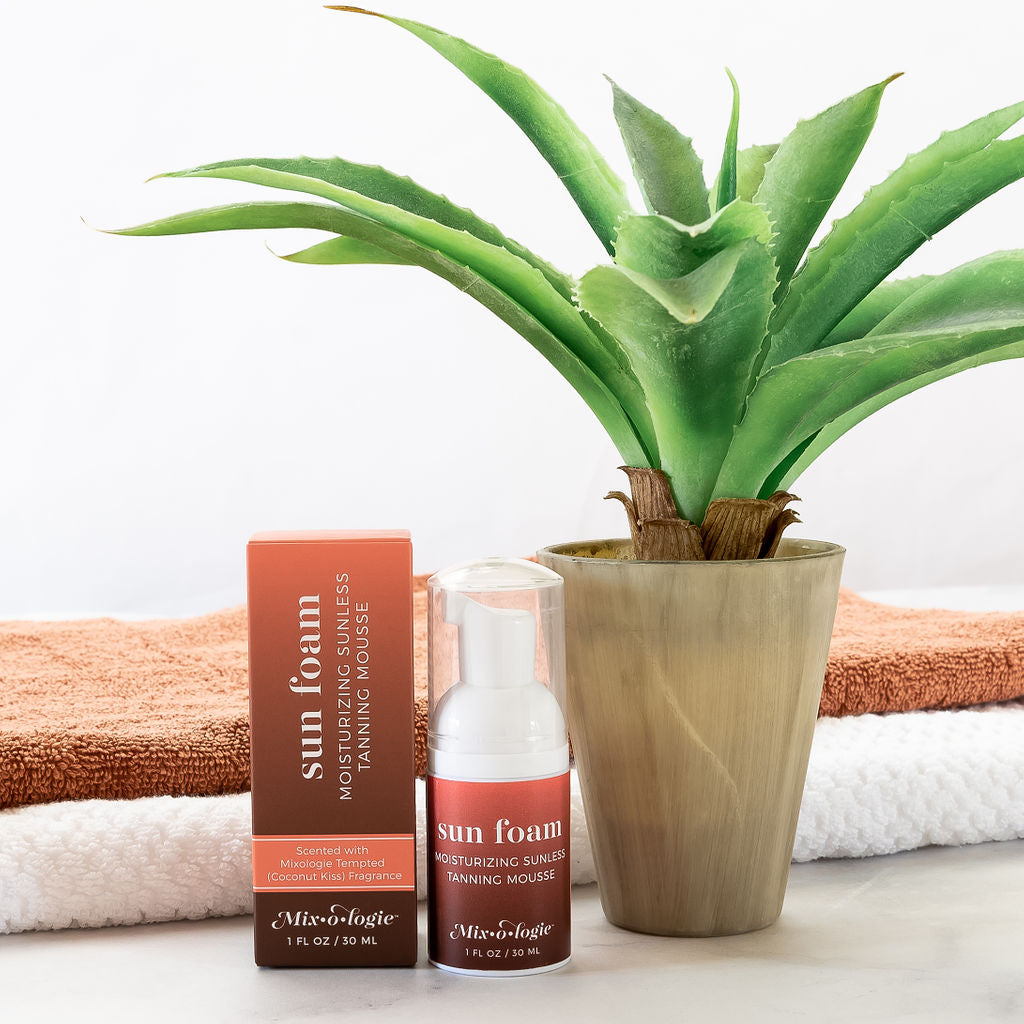 An aloe vera plant on a towel next to a box of Mixologie SunFoam Tanning Mousse cream.