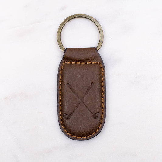 A Golf Leather Embossed Keychain in Dark Brown with the brand name of The Royal Standard and an image of two crossed baseball bats on it.