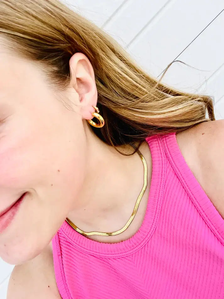 A girl wearing a pink top and gold hoop earrings.