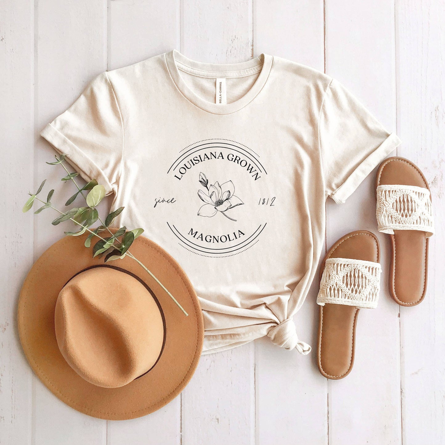 A Louisiana State Flower | Short Sleeve Graphic Tee by Olive And Ivory Wholesale, hat, and slippers are laid out on a white.