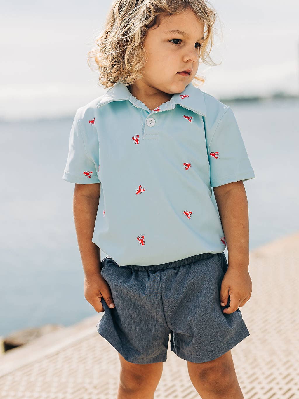 a little boy wearing a Sugar Bee Clothing Crawfish Polo Shirt and standing on a sidewalk.