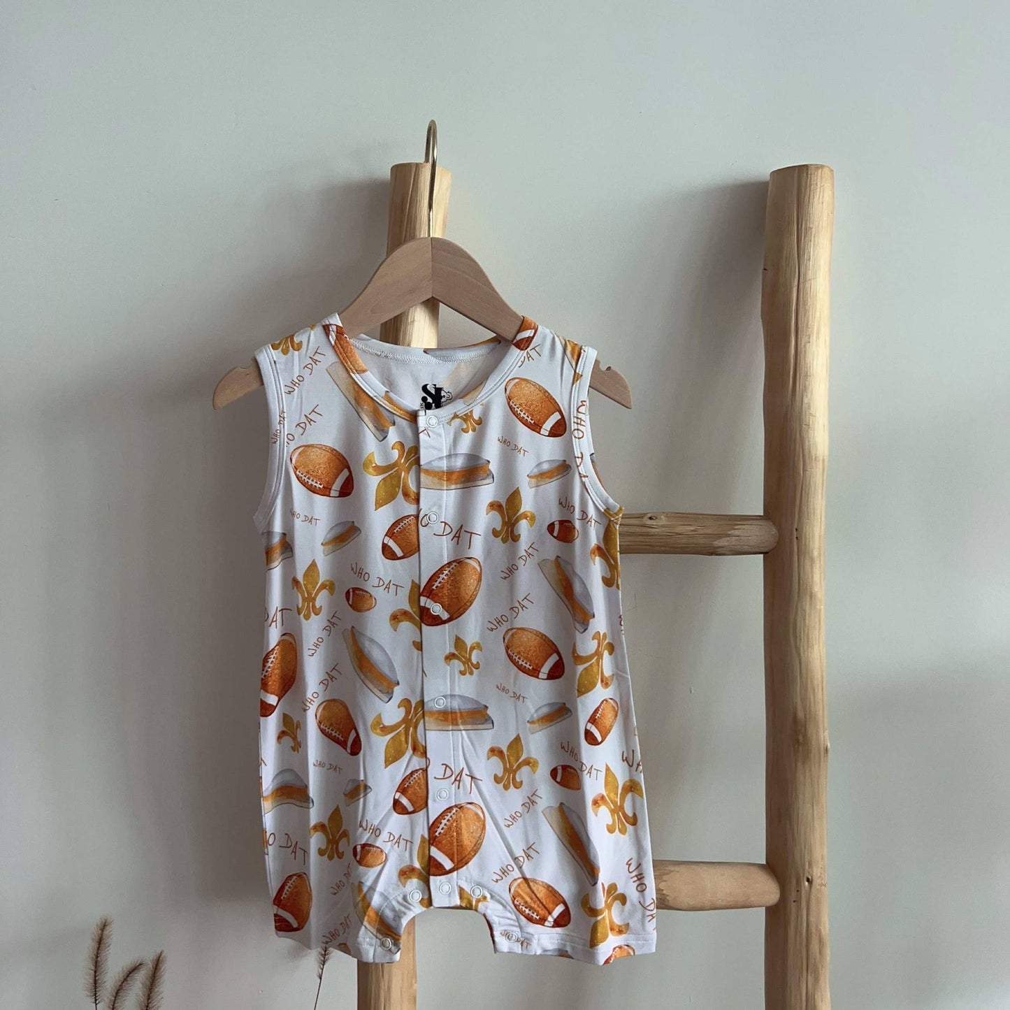 A child's Who Dat Football Bamboo Romper, made by SeersuckerJOEY LLC, hanging on a wooden ladder.