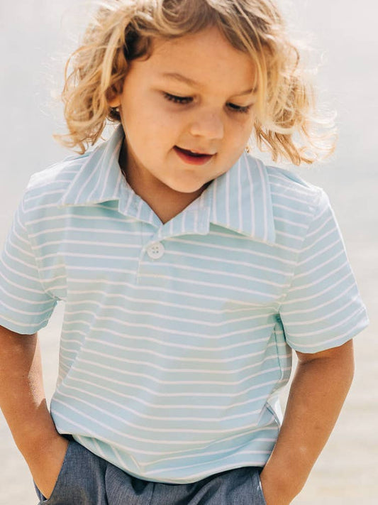 A little boy that is standing in the sand wearing a Sugar Bee Clothing Blue Stripe Polo Shirt.