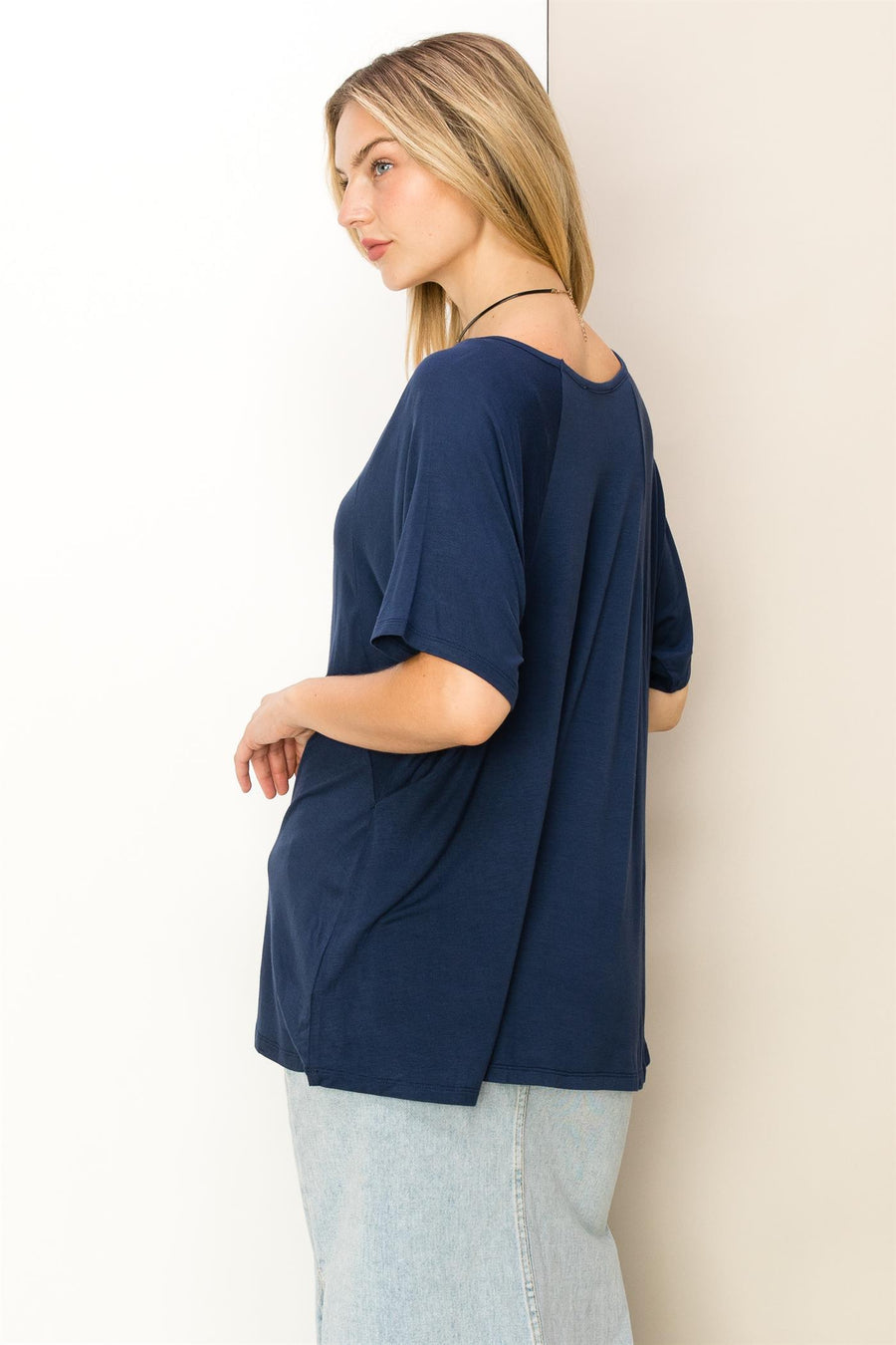 A woman standing against a wall wearing a HYFVE Oversized Short Sleeve Top in blue.