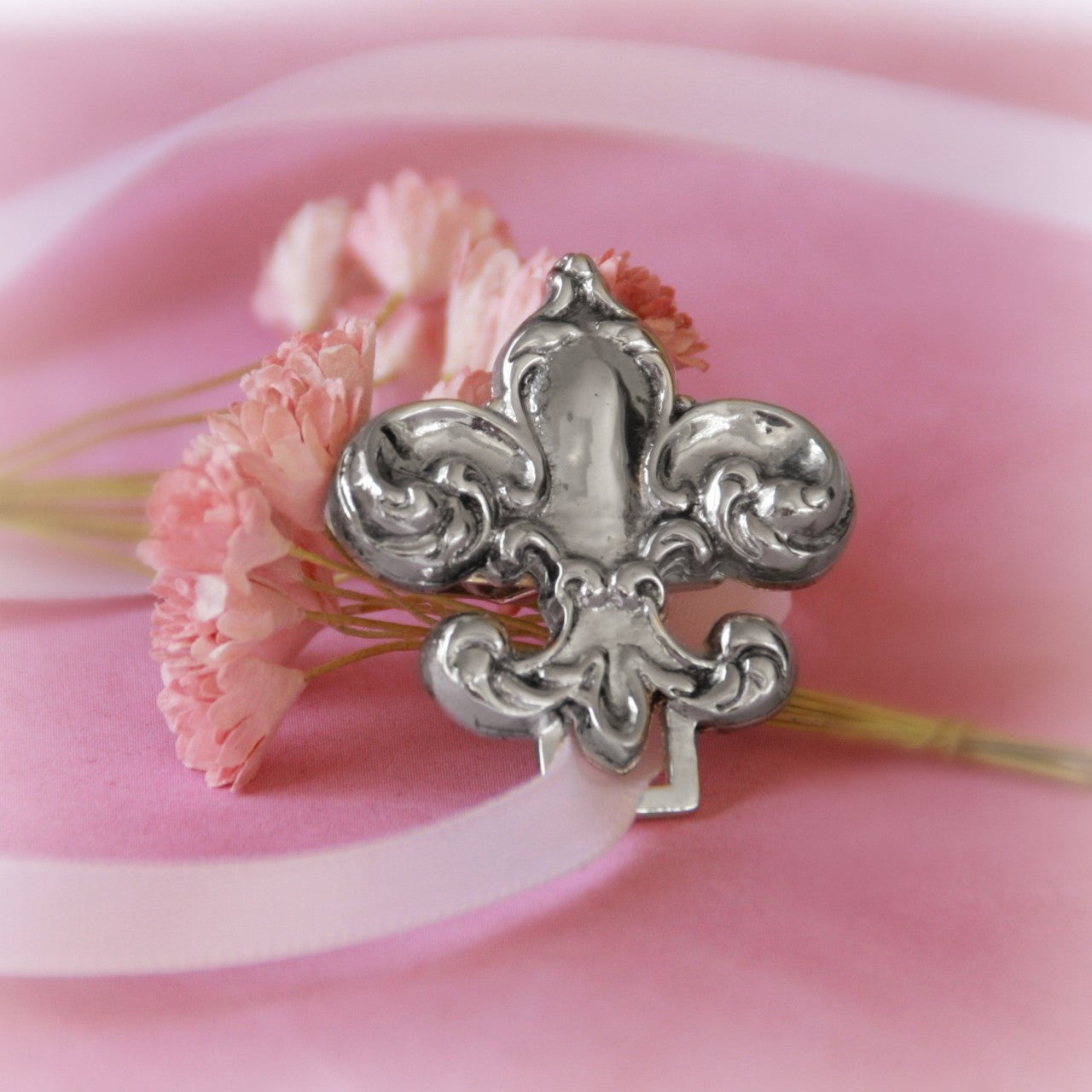 A pink flower and a silver Collectables America Fleur De Lis Paci Holder.