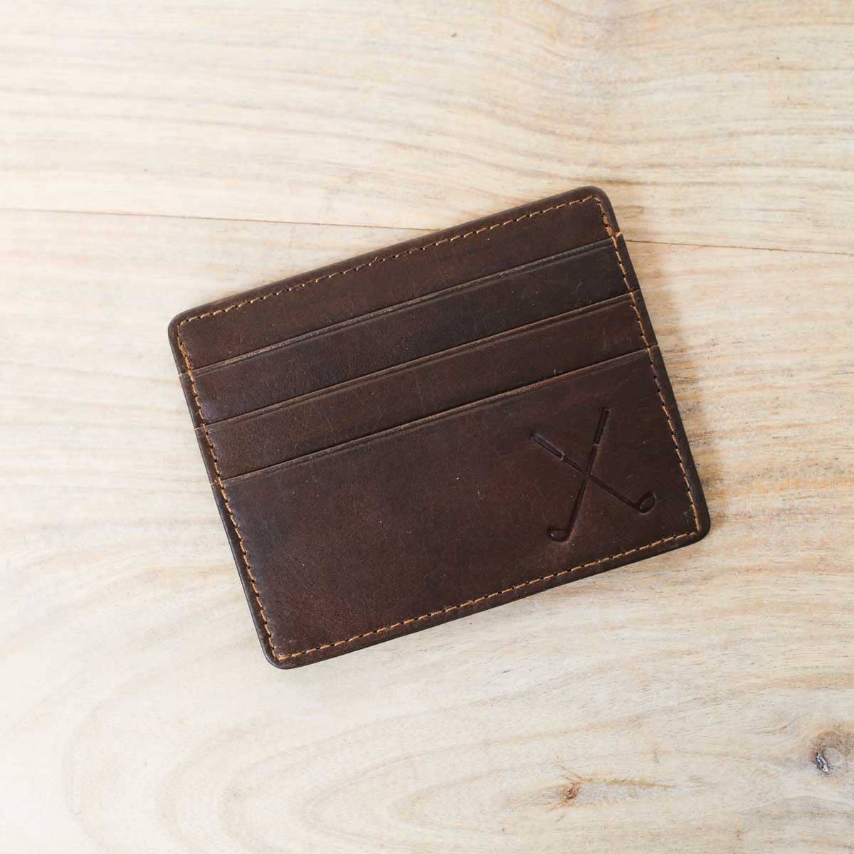 A Golf Leather Embossed Slim Wallet in Dark Brown from The Royal Standard sitting on top of a wooden table.