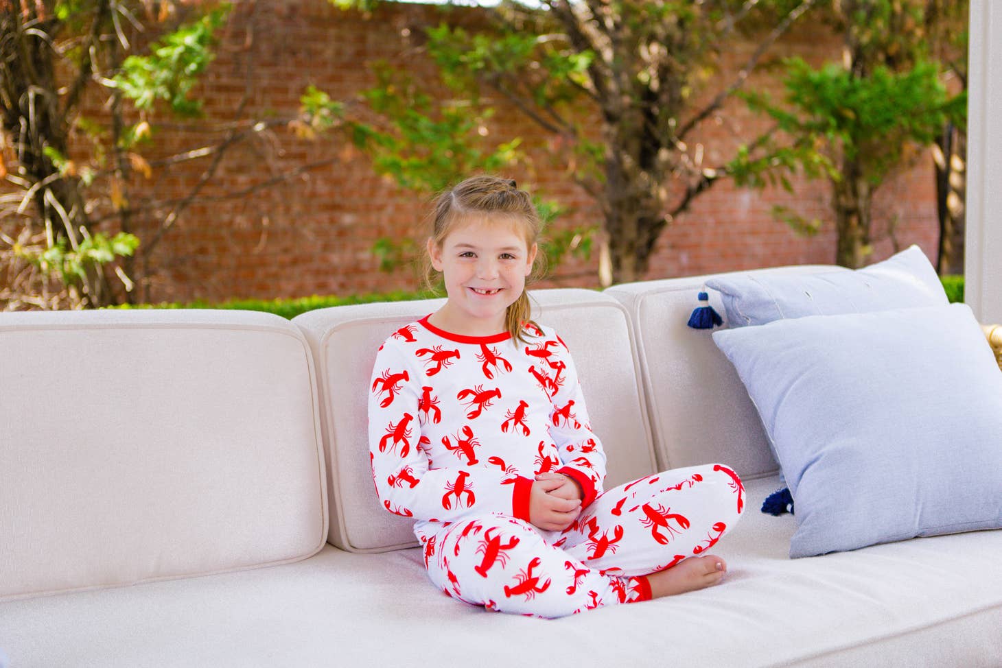 A little girl sitting on a couch wearing Sugar Bee Clothing's Crawfish Buttflap Pajamas.