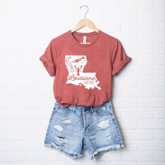 A Louisiana Vintage | Short Sleeve Graphic Tee by Olive And Ivory Wholesale hanging on a brick wall.