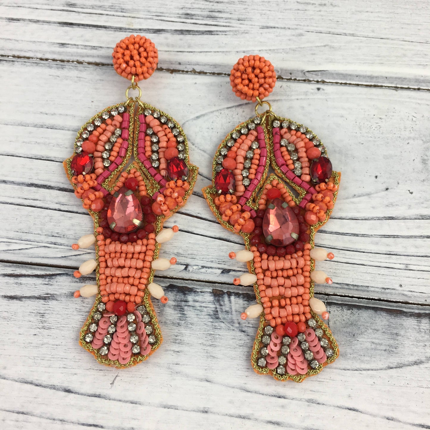 A pair of SongLily Bead and Stone Crawfish Earrings inspired by Mardi Gras on a wooden table.