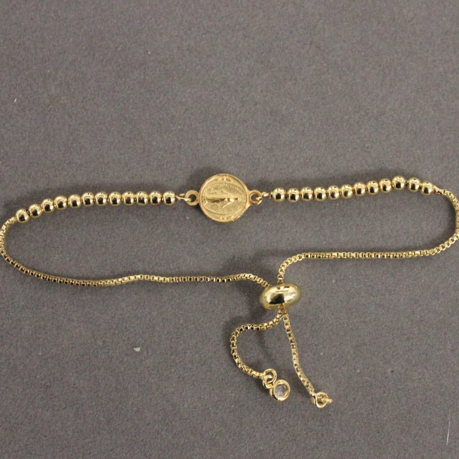 An Adjustable Virgin Mary Double Sided Gold Bead Bracelet by Weisinger Designs with a coin on it.